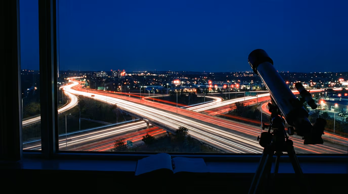 A telescope at a night window overlooking motorway light trails far below