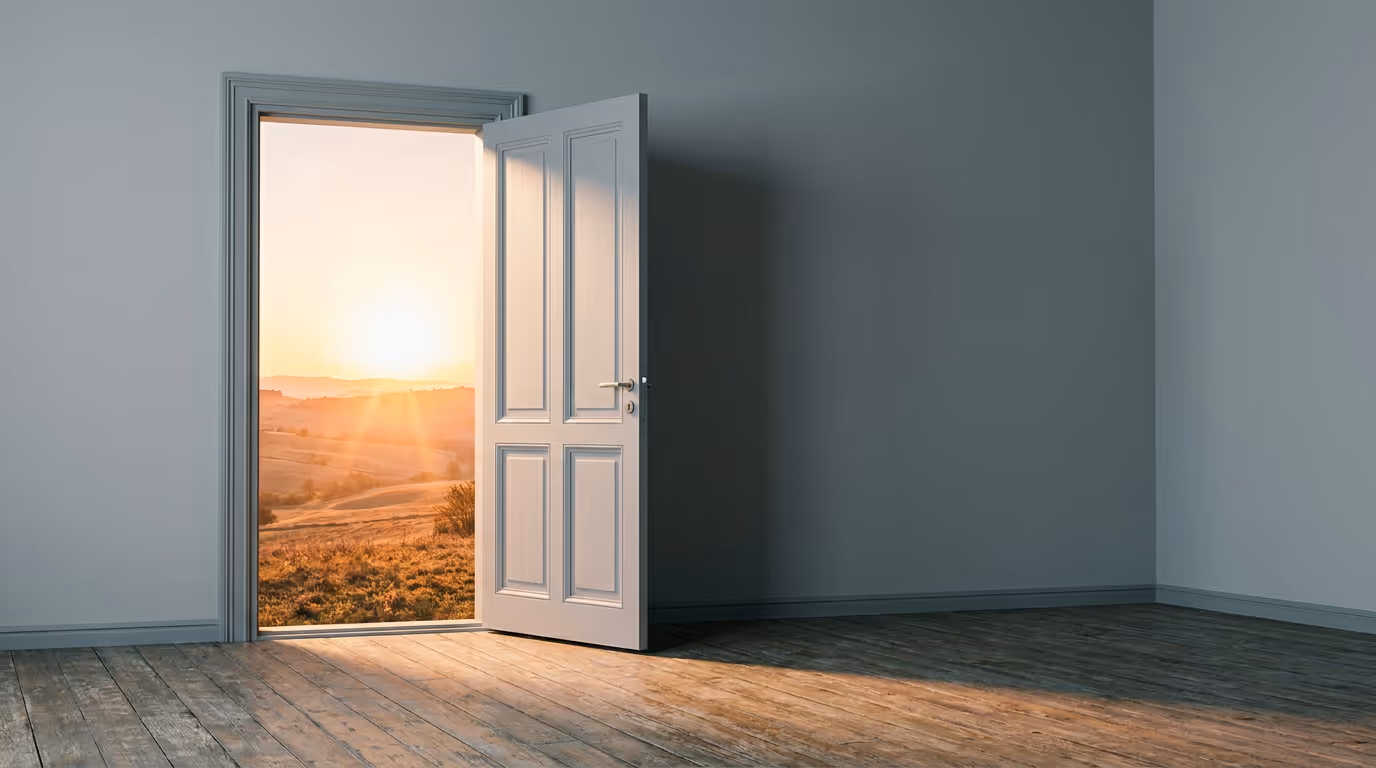 A door standing ajar in a plain room, opening onto a warm sunset landscape